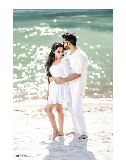 A romantic embrace on the beach, with the sun sparkling on the water behind them. The man gently kisses her forehead, creating a tender and beautiful moment.