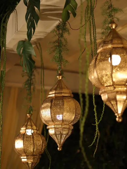 Golden Moroccan-style lanterns hanging amidst lush greenery, adding a warm and exotic glow to the decor.