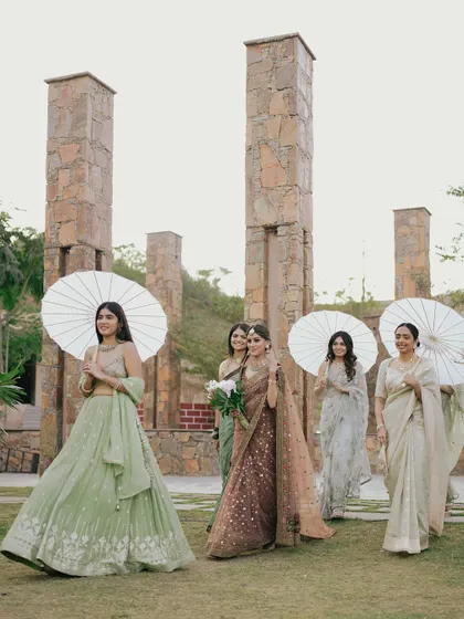 The bride, Mouli, makes her entrance with her bridesmaids, who are holding elegant paper umbrellas. This is a beautiful, coordinated moment from her Udaipur wedding.