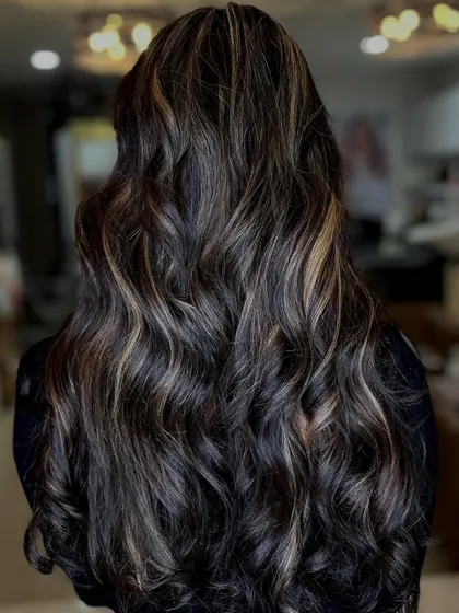 A gorgeous example of subtle balayage on dark, long hair. The highlights are delicately woven in to create a natural, sun-kissed look, styled in beautiful waves.