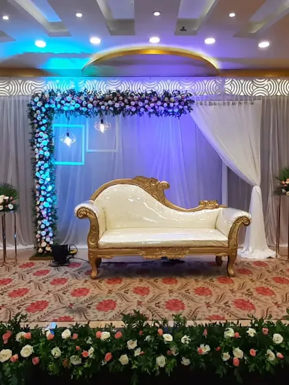 A modern engagement stage with an L-shaped floral frame, neon light accents, and a white chaise lounge.