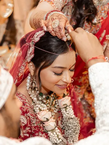 An intimate close-up of the sindoor ceremony, a pivotal and emotional moment in a Hindu wedding. The focus is on the gentle act and the bride's serene expression, capturing the sanctity of the ritual.