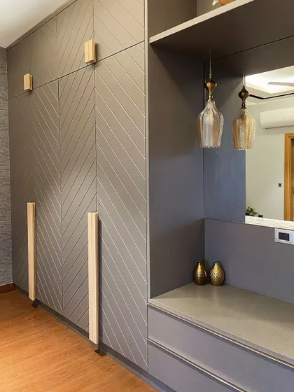A detail of a grey wardrobe with a chevron pattern and light wood handles. A small dresser nook with a mirror and pendant lights is seamlessly integrated into the design.