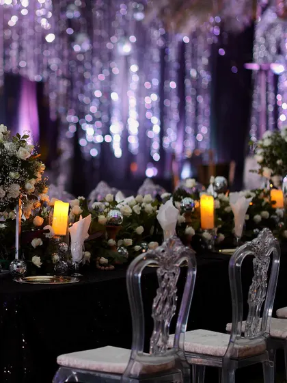 Guest seating at the enchanted forest party. The clear ghost chairs and sparkling table decor reflect the purple and white lights, adding to the shimmering, magical effect of the space.