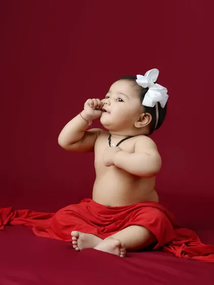 A classic baby portrait against a rich red backdrop. This image captures the innocent curiosity and sweet expression of a baby girl.