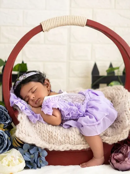 A full view of the newborn girl sleeping in a round basket surrounded by flowers. The composition creates a beautiful, artistic portrait.