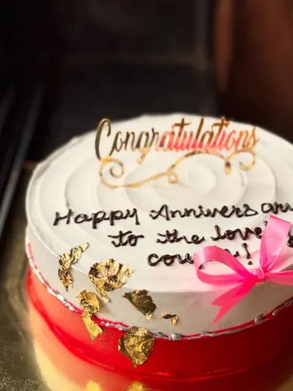 A simple and elegant anniversary cake with a "Congratulations" topper and gold leaf details.