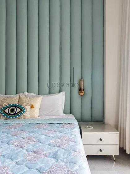A detail shot of the full-height upholstered headboard. The vertical panels add texture and a sense of height to the room, while the quirky evil eye cushion adds a personal touch.