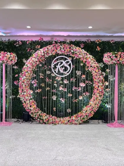 This engagement stage is a vision in pink and green. A large circular floral arrangement serves as the centerpiece, set against a lush green hedge wall for a fresh, garden-like feel.