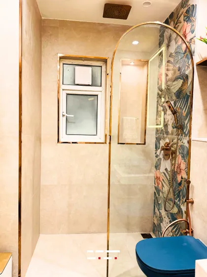 A stylish bathroom with a unique arched glass shower partition framed in gold. The tropical-print accent wall inside the shower adds a vibrant and unexpected design element.