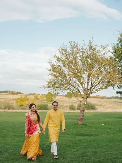A sunny Haldi ceremony in the British countryside, with details like "Love is all we need" henna, fresh yellow flowers, and bowls of rose petals.