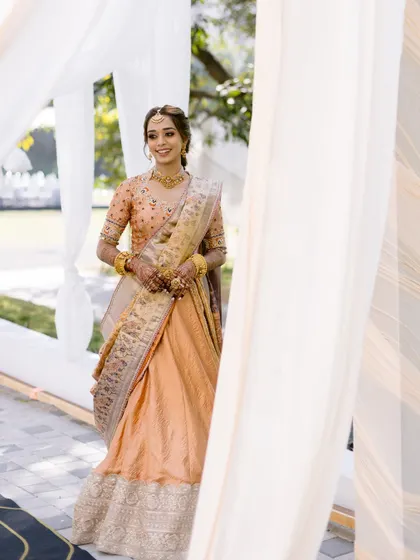 A full-length view of the bride, her smile as bright as the sunshine. The soft, elegant makeup is perfect for this outdoor haldi ceremony.