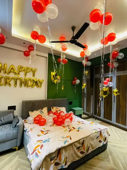A simple and sweet room decoration with red and white balloons on the ceiling and a gold "Happy Birthday" foil banner above the bed.
