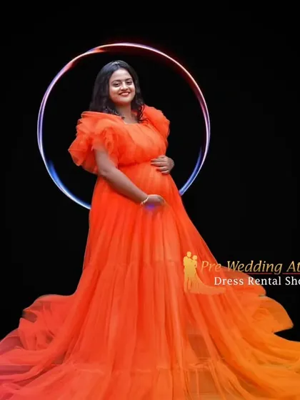 This bright orange ruffled gown is perfect for a modern and vibrant studio maternity shoot. The voluminous tulle skirt and ruffled shoulders create a high-fashion look against a simple black background.