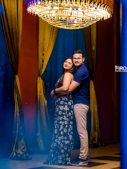 An elegant indoor portrait under a grand chandelier. The warm lighting and rich blue curtains create a sophisticated and classic look.