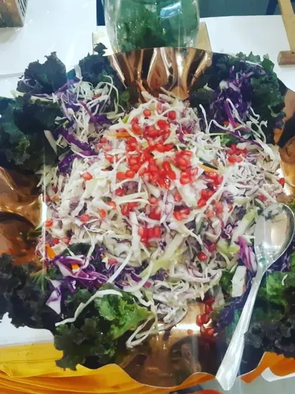 A creamy coleslaw salad topped with bright red pomegranate seeds, served on a bed of purple lettuce.