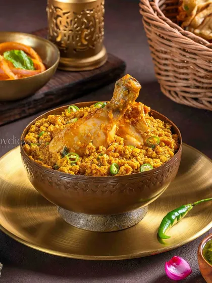 Chicken Keema Biryani, with a whole chicken leg on top, served in a traditional brass bowl with green chutney.