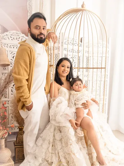 A stylish family portrait with a boho-chic theme. The parents and their baby are posed in and around an elegant golden birdcage chair.