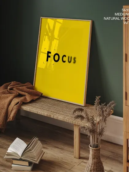 This image shows the "FOCUS" print in a natural wood frame with a glass cover, creating a clean and polished look. The reflective surface adds a touch of elegance to the modern design.