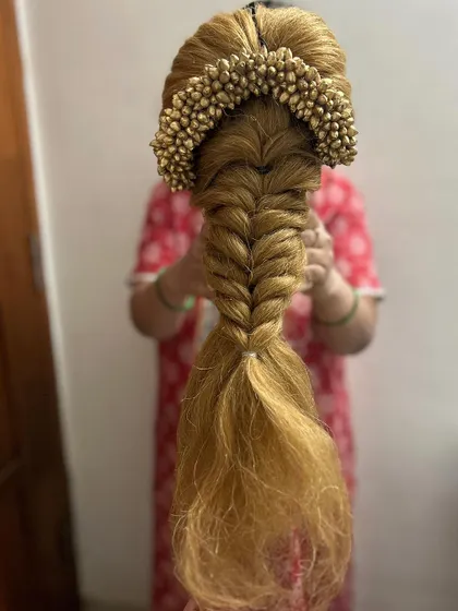 A fishtail braid paired with a golden floral accessory, created on a mannequin head. This is a great example of how we practice combining traditional and modern elements in my hair education classes.