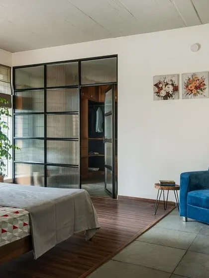 This bedroom features a walk-in wardrobe separated by a fluted glass and metal partition. This solution provides privacy while allowing light to filter through, making the space feel larger.