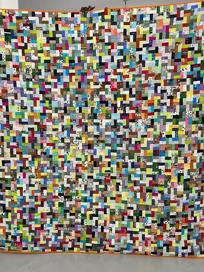 A full view of an incredibly detailed and colorful scrappy quilt, a testament to using every last piece of fabric.