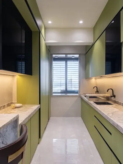 This angle highlights the parallel counter layout of the Kalyan kitchen, providing ample workspace. The design incorporates black matte fixtures and profile handles for a sharp, contemporary contrast against the green cabinets.