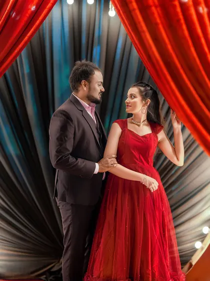 A dramatic and intimate portrait of a couple framed by rich red curtains, creating a theatrical and cinematic feel.