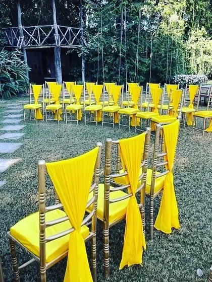 Bright yellow chair decorations for an outdoor Haldi ceremony. Coordinating the seating with the main decor theme ties the whole event together beautifully.