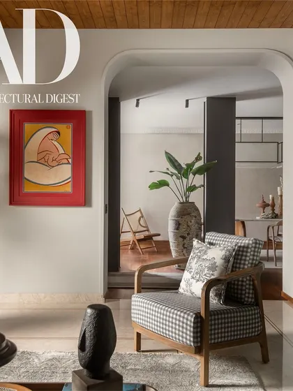 An arched entryway frames a view into the living space, where a checkered armchair and a Jamini Roy painting add personality. The wooden ceiling and marble floors provide a rich textural contrast.