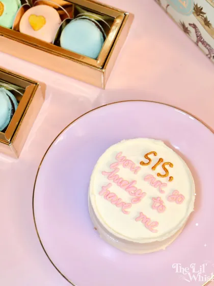 A beautifully styled shot of our Rakhi collection, featuring a sassy bento cake and a box of our custom "Sis" macarons. It's the perfect combination for a sweet and memorable gift.