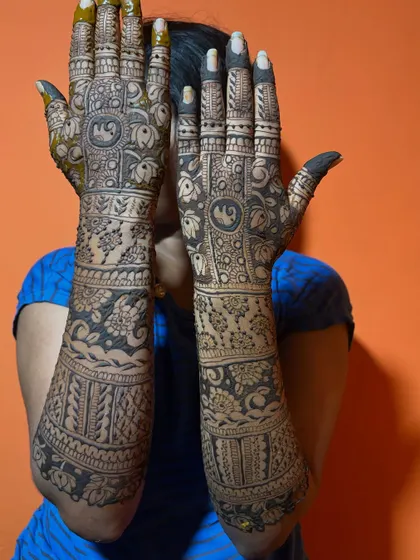A full-coverage bridal mehendi with elephant motifs and lotus patterns. The bride is playfully hiding her face, letting the intricate henna art take center stage.