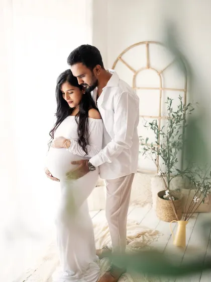 A sweet and gentle moment between the parents-to-be. He stands behind her, wrapping his arms around her and the baby bump in a protective and loving embrace.
