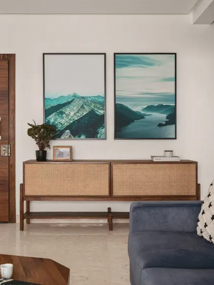 This simple and elegant setup features a beautiful rattan console that adds natural texture to the room. The large landscape art pieces bring a sense of calm and a connection to nature, creating a serene and welcoming entryway or living room corner.