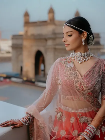 A modern take on the red bridal look, set against the iconic Gateway of India. Her makeup is clean and elegant, with a focus on radiant skin and a simple bindi, letting her natural beauty and the stunning view shine.