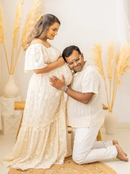 Listening for the first hellos. The father-to-be kneels and rests his ear against his partner's belly, a classic and heartwarming pose that we captured during their boho-themed studio maternity session.