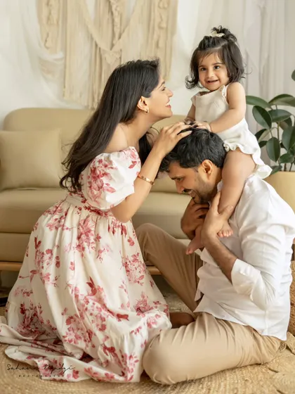 A playful family moment, with the daughter sitting on her father's shoulders while her mother looks on with love. A beautiful, interactive family portrait.