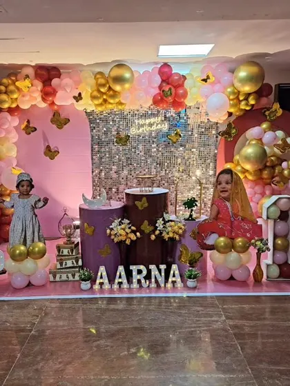 Aarna's first birthday was celebrated with this lovely butterfly theme. The setup includes a pink and gold balloon arch, a sequin backdrop, and life-size photo cutouts of the birthday girl.