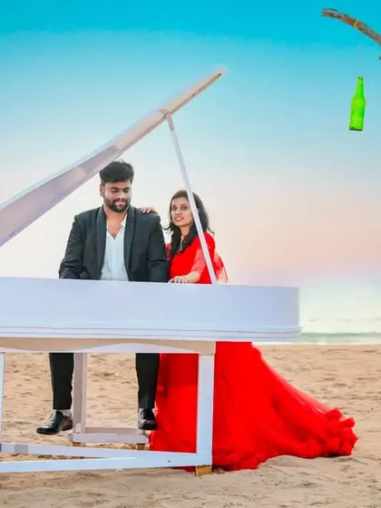 A whimsical beach setup with a piano on the sand. The couple's outfits, a red gown and a black suit, add to the surreal and romantic atmosphere.