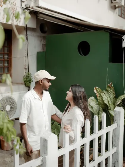 Another angle from a charming pre-wedding shoot, capturing the couple's interaction near a white picket fence.