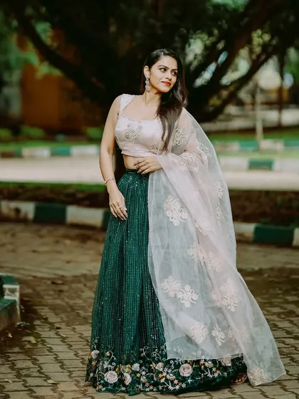 A model wearing a beautiful dark green and blush pink lehenga. The sequined green skirt is paired with a simple pink blouse and an embroidered net dupatta.