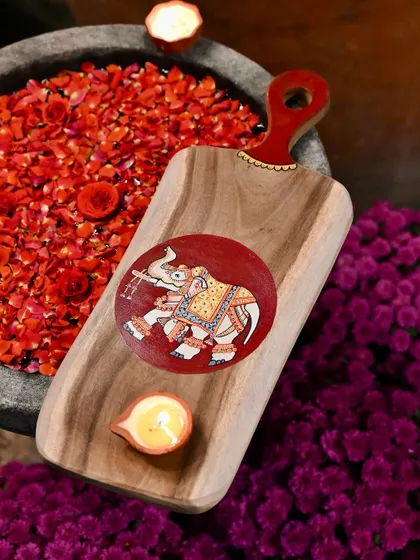 This hand-painted wooden platter, featuring a decorated elephant, is a perfect piece for festive decor. Placed in an uruli with flowers, it becomes a beautiful and traditional centerpiece.