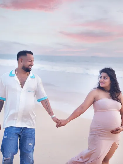 A romantic walk along the shore. This beach maternity session captures the couple hand-in-hand against a beautiful pastel sunset sky, creating a serene and picturesque memory.