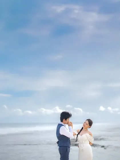 A gentle kiss on the hand with the vast Bali coastline behind you. This wide shot captures both the intimate gesture and the epic scale of the destination.
