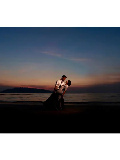 A dramatic pre-wedding photo of a couple in a dance pose on the beach at dusk. The deep blue and orange hues of the sky create a cinematic and romantic atmosphere.