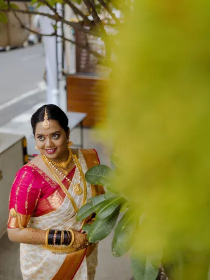 A portrait of a bride on her muhurtham day, smiling warmly in her beautiful white and red saree.