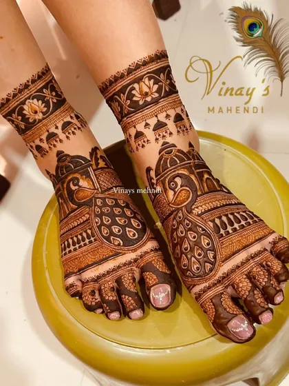 An elegant feet design with peacocks and jhumkas, perfect for a bride. The photo is taken on a yellow stool, which makes the henna color pop.