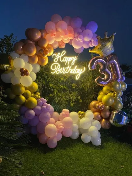 An outdoor 31st birthday ring setup with a colorful assortment of pastel and metallic balloons, a neon sign, and a crown foil balloon.