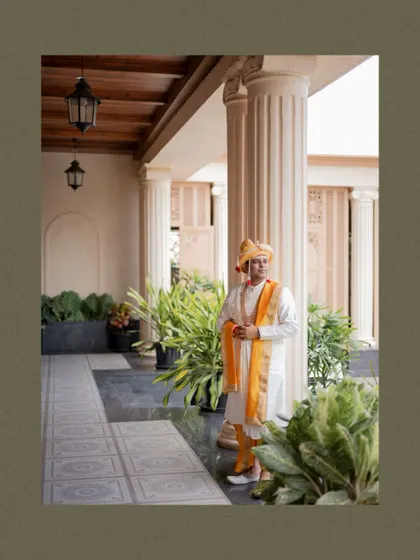 A wide portrait of the groom standing in a beautiful arched hallway, showcasing the grandeur of the wedding venue.