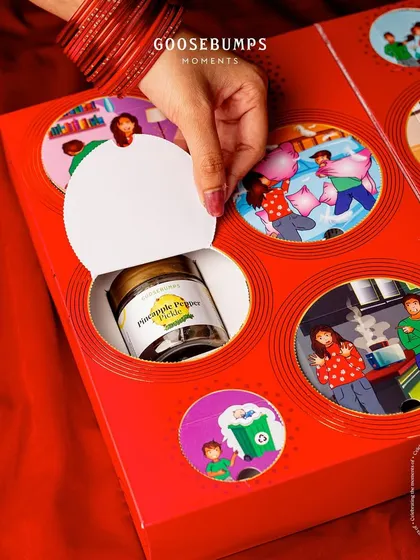 Tearing open another memory. This image shows a jar of my unique Pineapple Pepper Pickle being revealed from behind a nostalgic illustration on the Rakhi gift box.